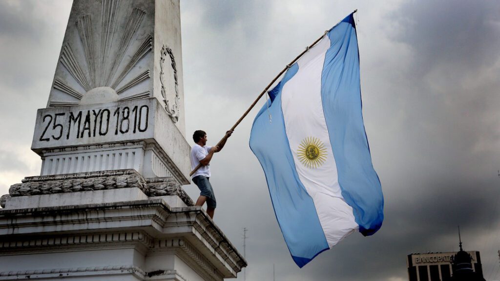 Manifestante con bandera argentina en la torre de plaza de mayo